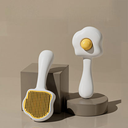 A pet fur brush designed to resemble an egg, with a white handle and yellow bristles, displayed on a beige background.